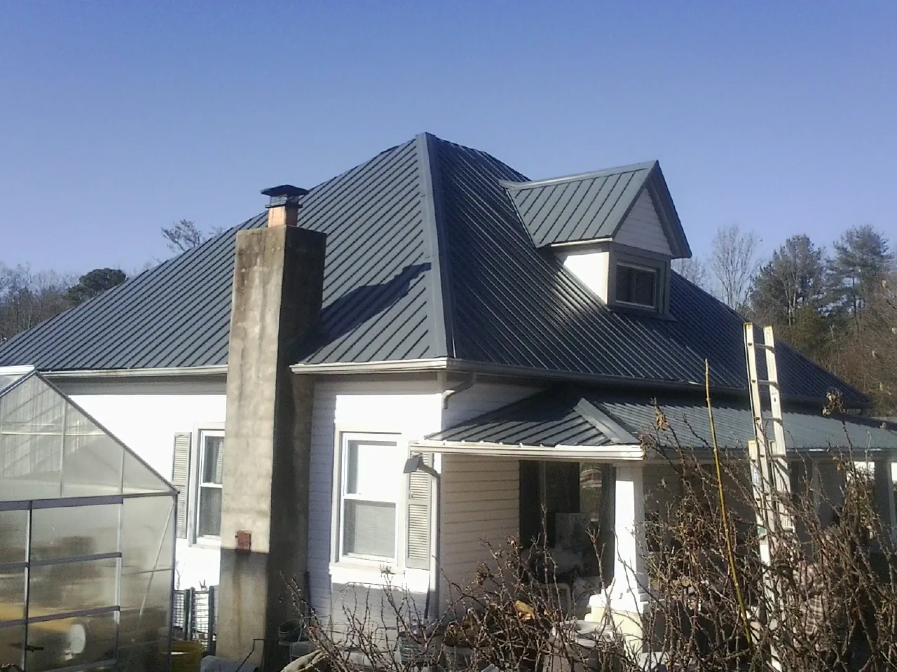 Dark blue standing seam metal roof on a white farmhouse with dormer in Beaver