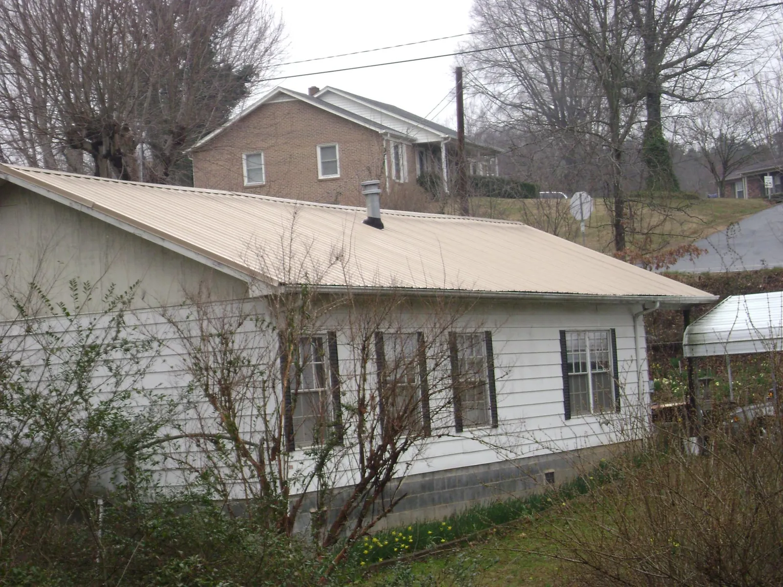 Tan metal roof on a white sided house set into a hillside — Commercial Roofing by Roofing Brothers in Beaver
